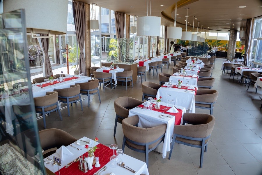 A Chapter Two table set with a red runner, fresh rose in a glass vase and folded napkins, entrance and buffet visible beyond