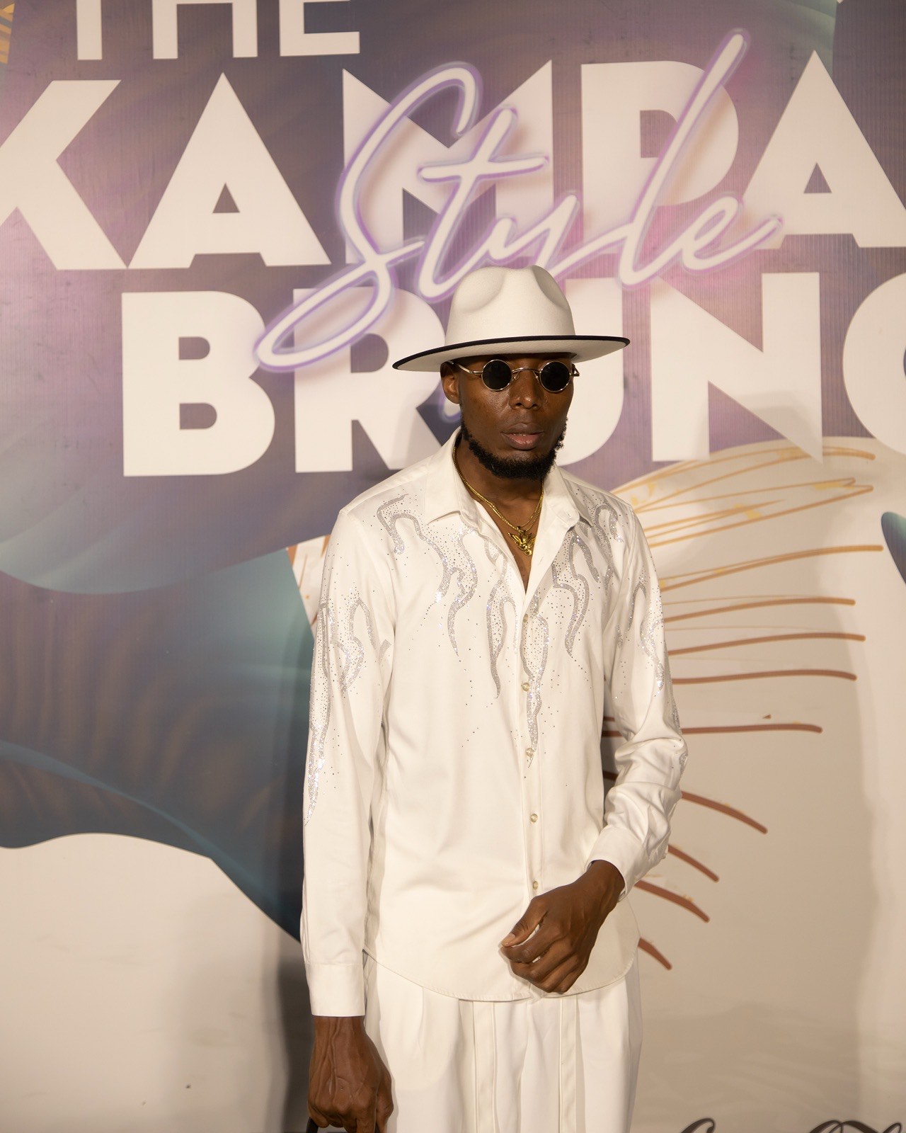 A guest in a statement white outfit poses at The Kampala Style Brunch backdrop, May 2024