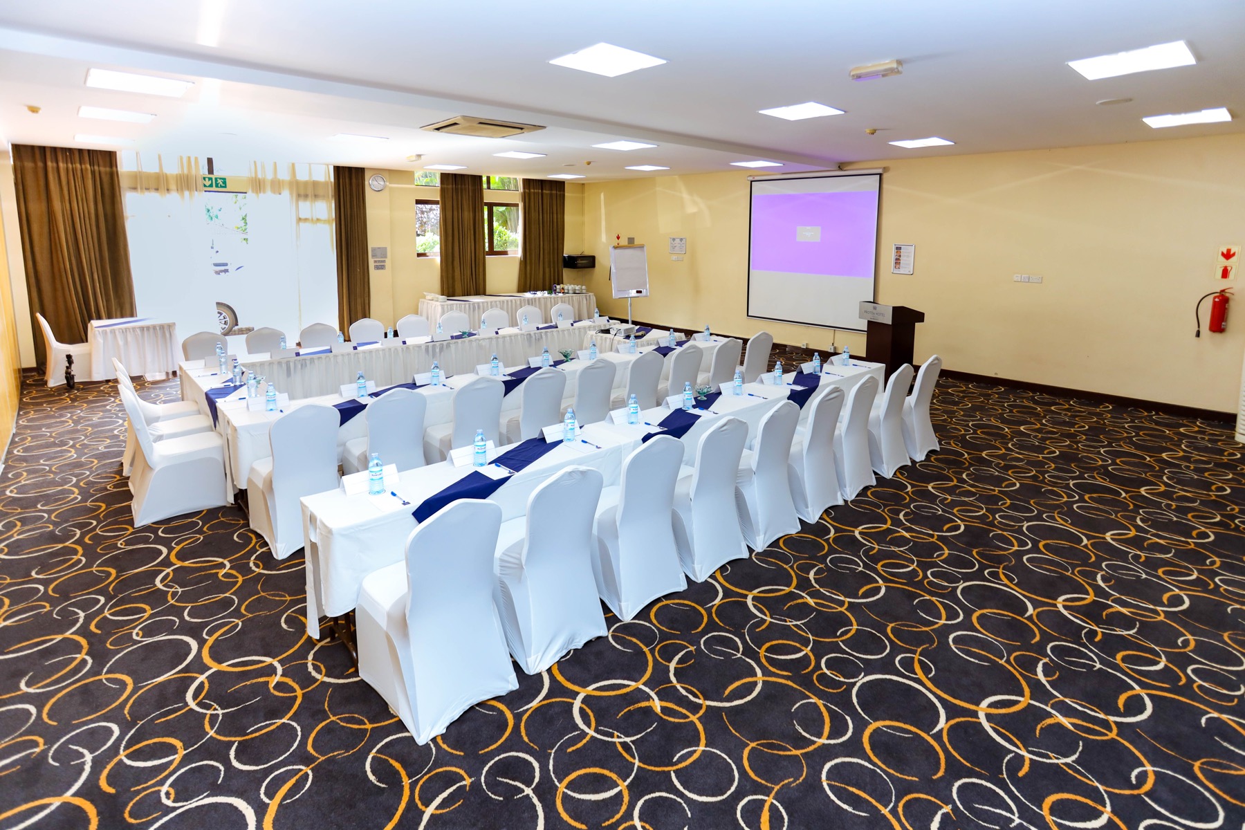 A Skyz Hotel Kampala meeting room set up classroom-style facing a projector screen