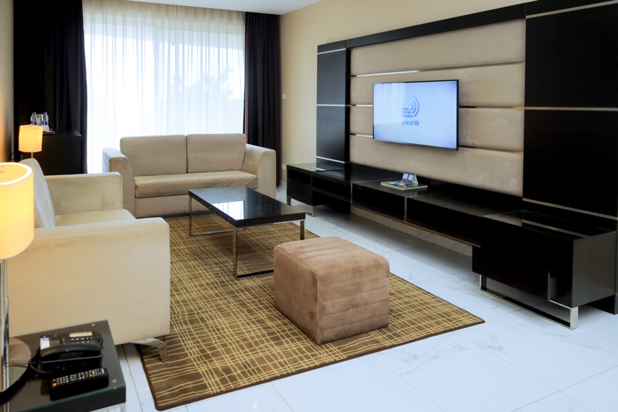 Separate living area in a One Bedroom Suite at Skyz Hotel Kampala, with cream sofas, a wall-mounted TV and patterned area rug